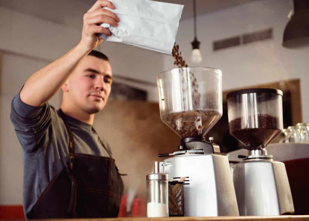 barista pouring coffee beans into grinder