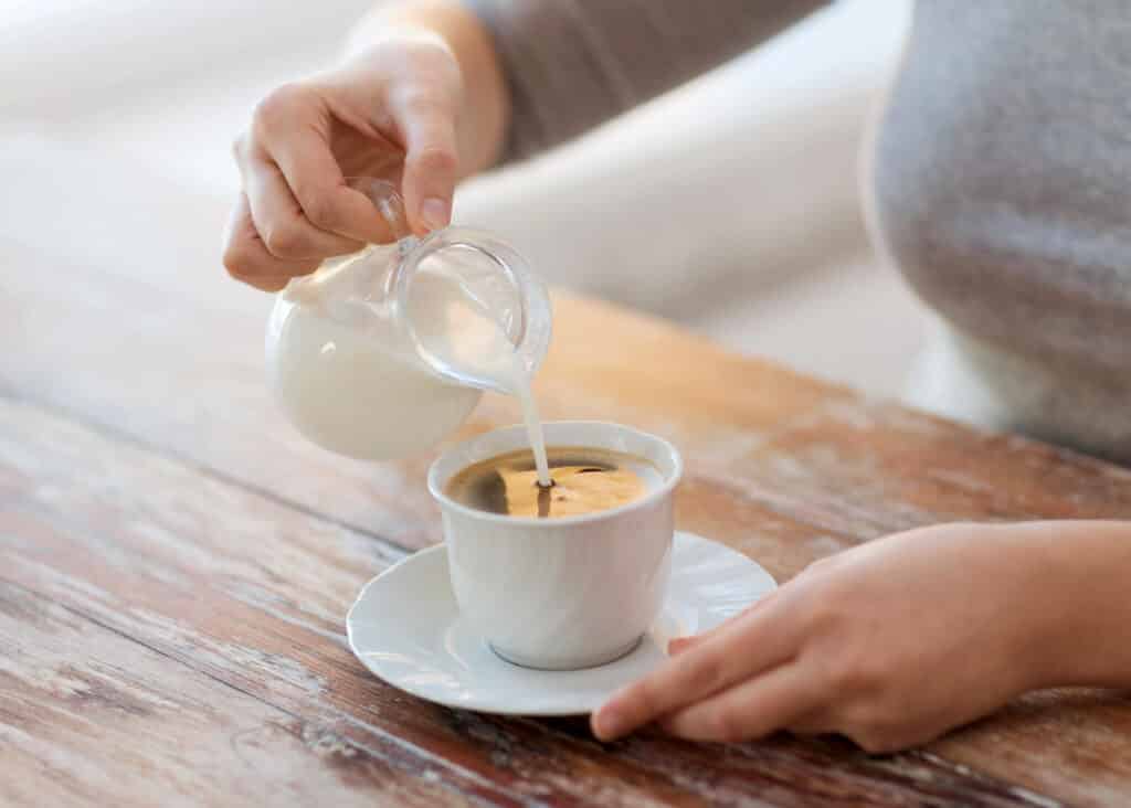 woman pouring milk into coffee