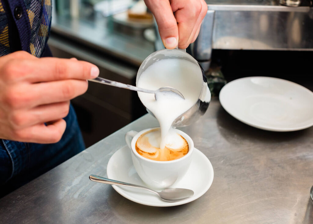 pouring frothed milk into coffee