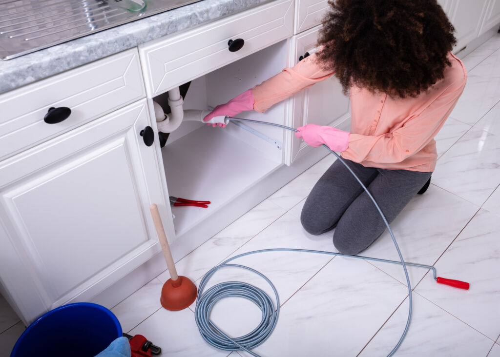 woman unclogging kitchen sink with drain snake