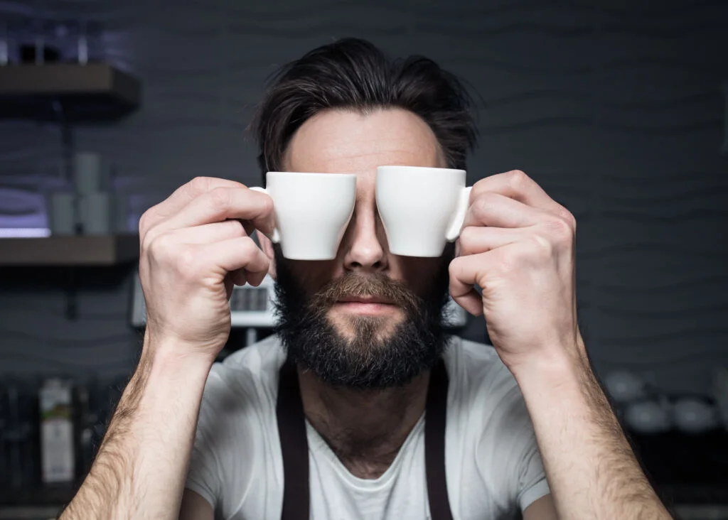 man covering his eyes with two espresso cups